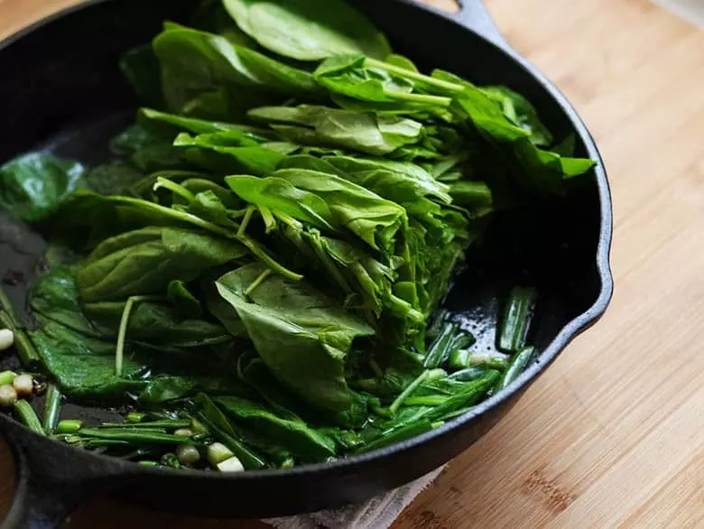 Fresh spinach frying in a pan with onions, salt and pepper.