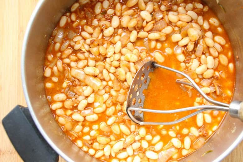 Large soup pot with bean masher mashing the beans.