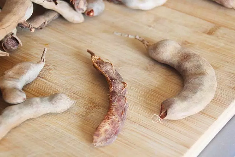 A peeled tamarind pod on the left and and un-peeled tamarind pod on a cutting board.