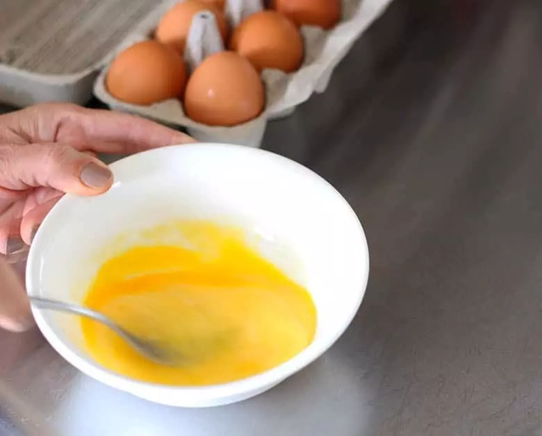 Eggs being whisked in a white bowl.