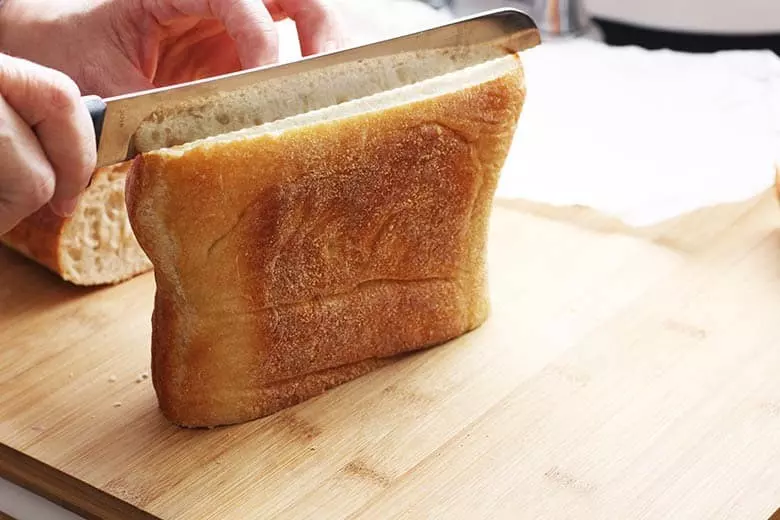 Ciabatta bread being cut lengthwise on a cutting board.