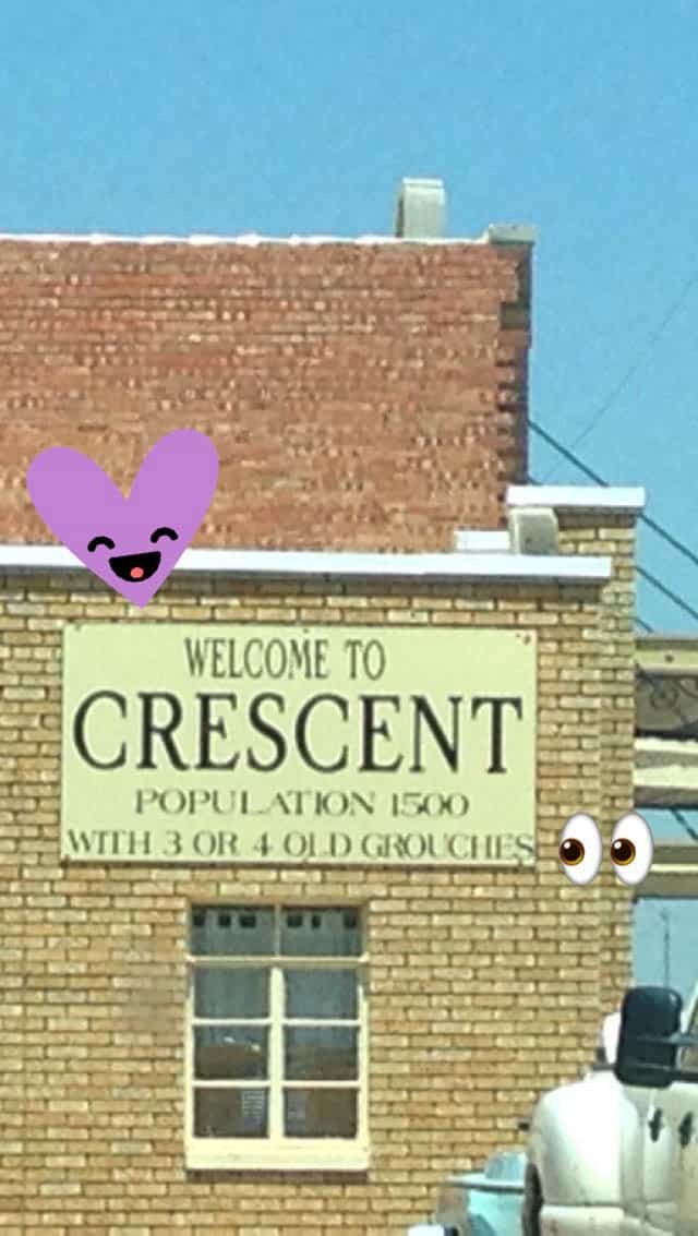 A sign on the side of the building that states "Welcome to Crescent - population 1500 with 3 or 4 old grouches."