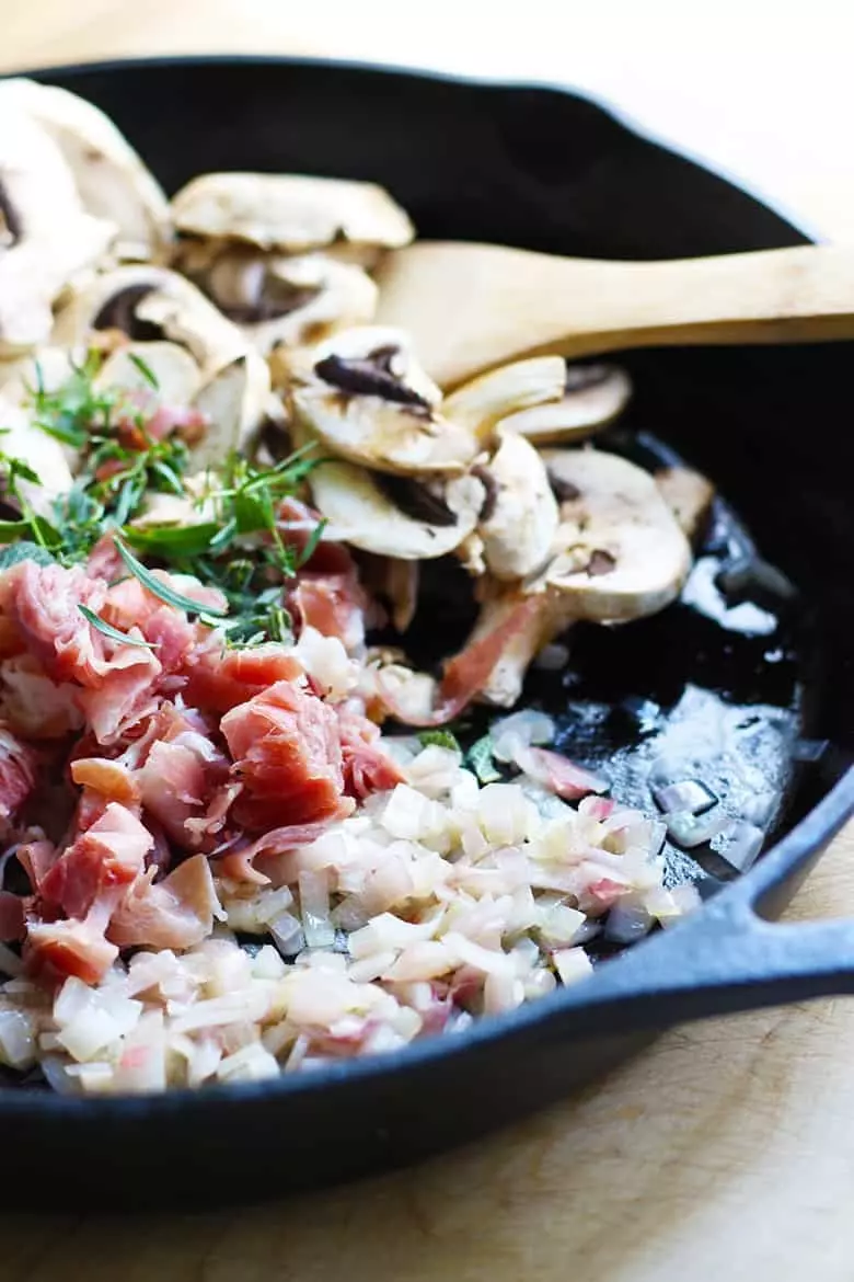 Mushrooms, herbs, onions and prosciutto in a cast iron skillet.