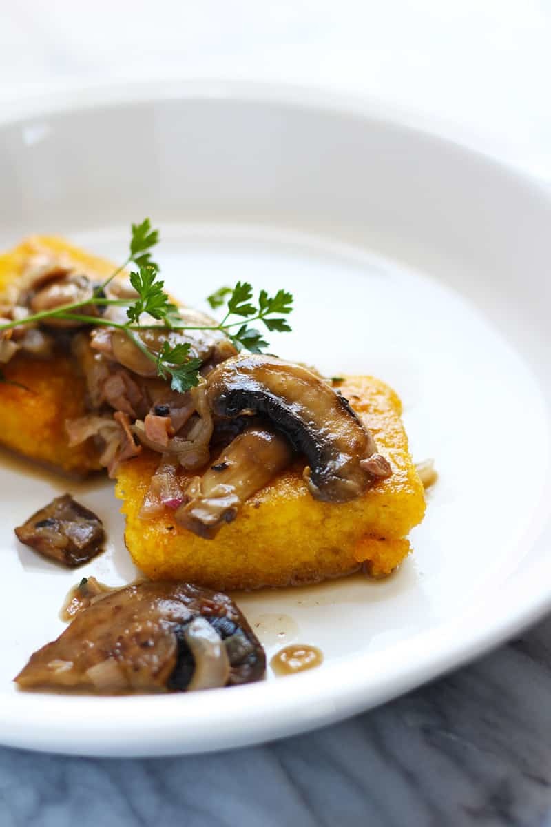 Fried polenta cake on a plate with mushrooms.
