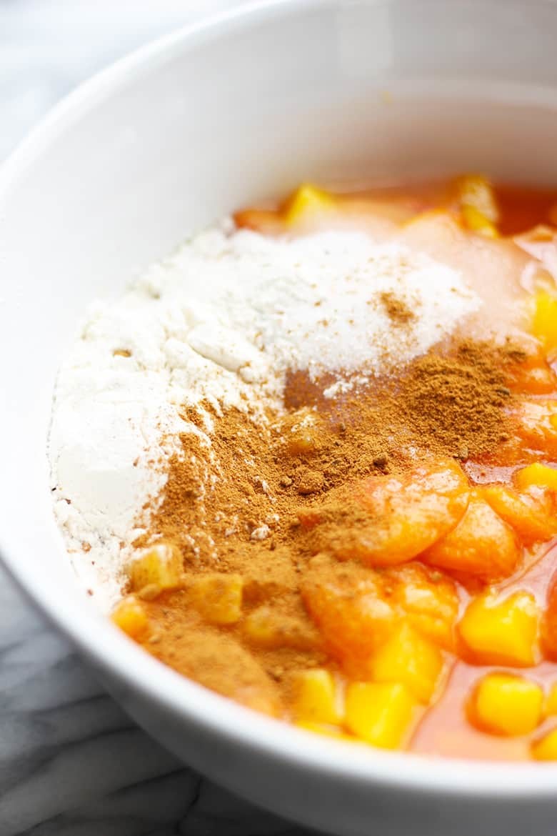 A white bowl with peaches, cinnamon and flour.
