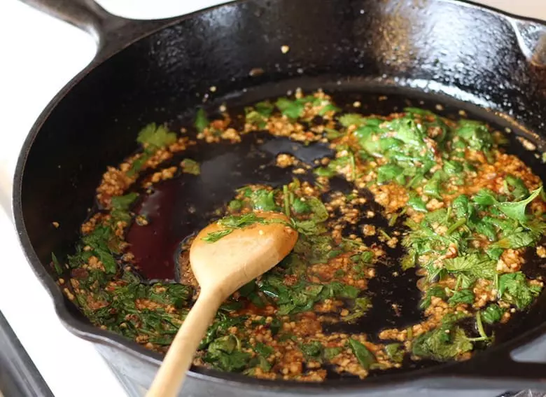 Stirring cilantro in a skillet with garlic.
