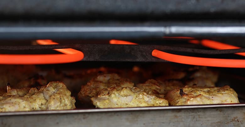 Chicken on a roasting pan under a broiler.