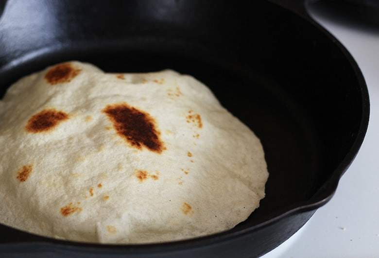 A tortilla cooking in a cast iron skillet.
