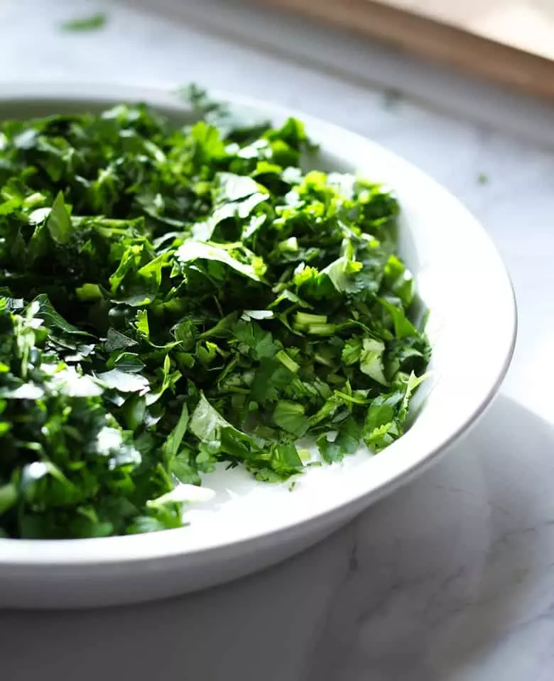 A white plate full of chopped green herbs.