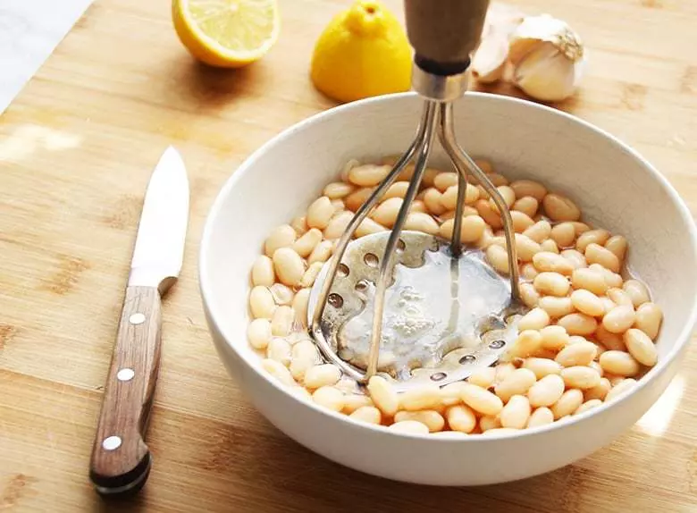 A bowl of white beans being smashed by a bean smasher.