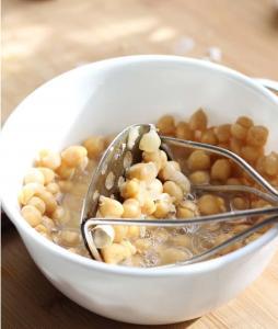 A bowl of chickpeas being smashed by a bean smasher.