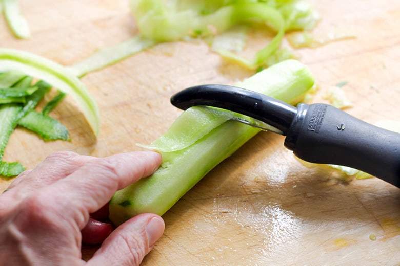 Slicing cucumber with a vegetable peeler.