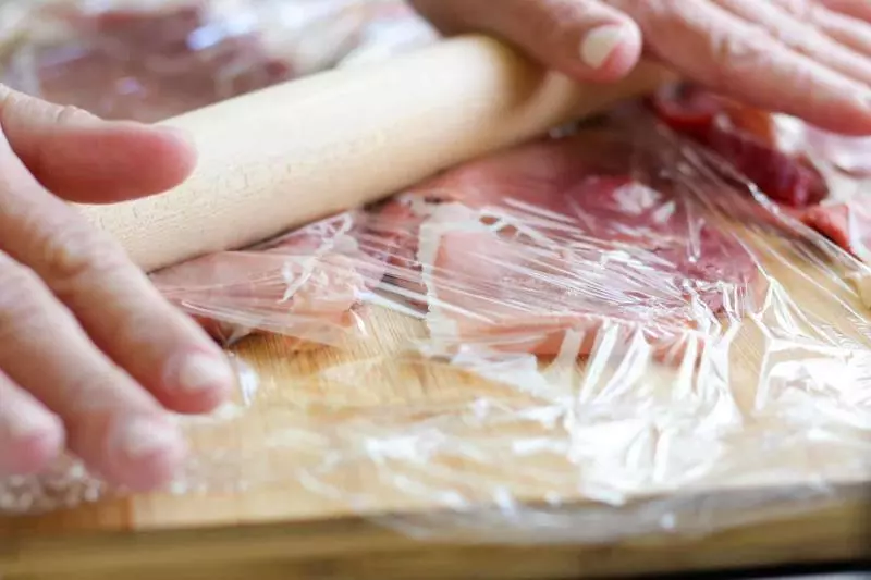 Rolling out meat with a rolling pin.