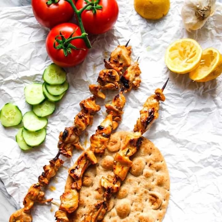 Shish Taouk on skewers with tomatoes, cucumber and lemon.