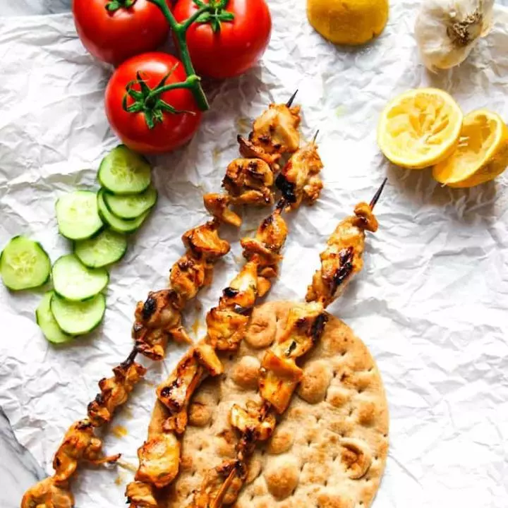 Shish Taouk on skewers with tomatoes, cucumber and lemon.