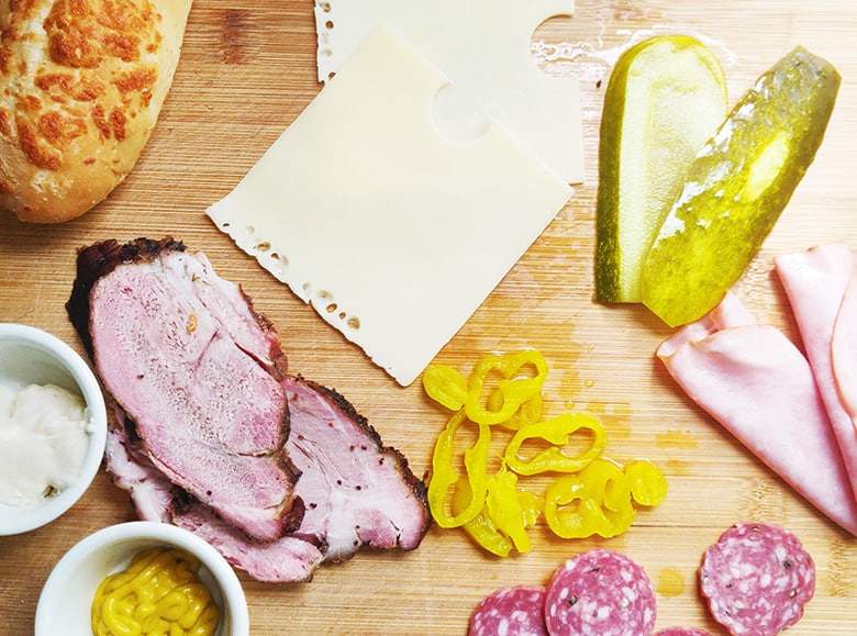 Pork, ham, salami, cheese, pickles on a cutting board.