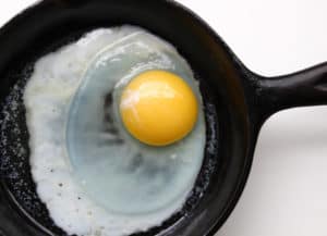 Single egg cooking in a black skillet.