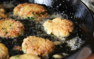 Salmon Croquettes frying in a cast iron skillet.