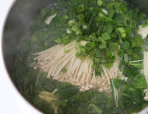 A pot with the mushrooms and scallions added to the rest of the ingredients.