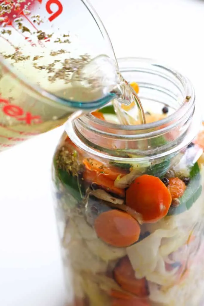 Pouring water into mason jar full of vegetables.