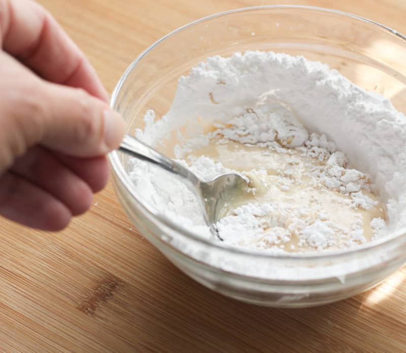 Stirring water and vanilla into powdered sugar.